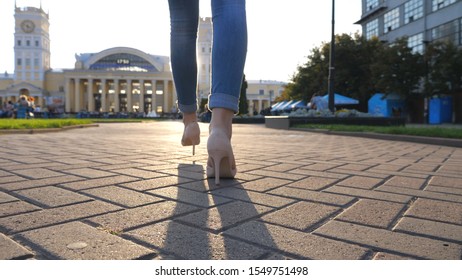 Female Legs In High Heels Shoes Walking Through Urban Street At Sunny Day. Confident Girl Stepping At Sidewalk With Cityscape At Background. Attractive Lady Having Stroll In City Environment. Slow Mo