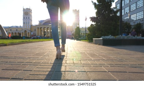 Female Legs In High Heels Shoes Walking Through Urban Street. Confident Girl Stepping At Sidewalk With Sunset At Background. Attractive Brunette With Red Bag Having Stroll In City Environment. Slow Mo