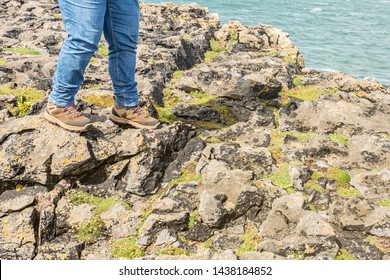 Female legs in jeans and feet in brown hiking boots walking on rocky shoreline rocks in the Burren, sea waters in the background, spring day in County Clare in Ireland. Wild Atlantic Way - Powered by Shutterstock