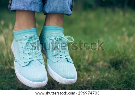 Female legs in jeans and sport shoe floating in the air above the green grass in the park. Flying sneakers outdoors. Conceptual image.