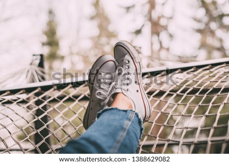 female legs in jeans and white sneakers on a hammock
