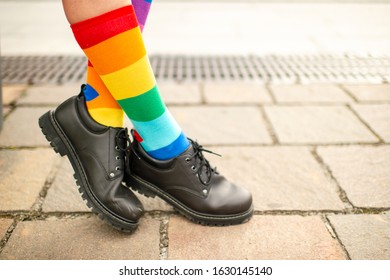 female legs in lgbt rainbow socks wearing male boots.