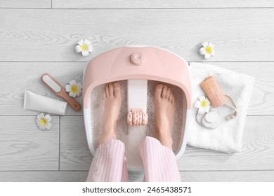 Female legs with massage foot bath and spa supplies on light floor - Powered by Shutterstock