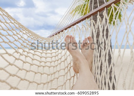 Female legs on hammock on tropical beach.