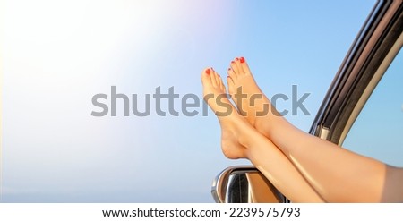 Female legs out of a car window on a background of sky. Holidays - relaxation.