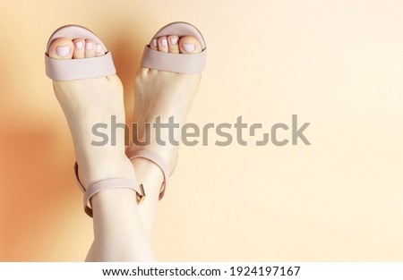 Female legs with pedicure in brown sandals on brown background, copy space