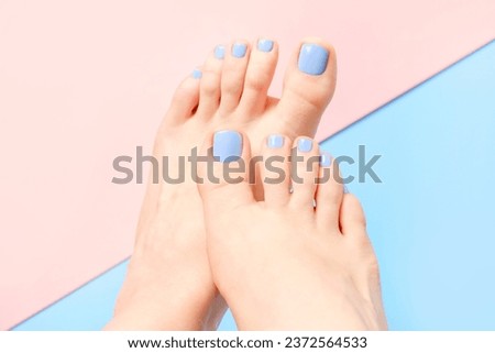 Female legs with pedicure on a pink and blue background.