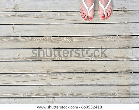 Female legs with a pedicure and sandals on the beach path of boards