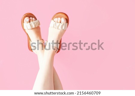 Female legs with pedicure in summer brown sandals on a pink background, copy space.