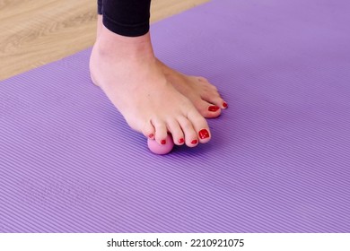 Female Legs With Red Nails Roll A Small Sports Ball On The Floor. On A Purple Yoga Mat