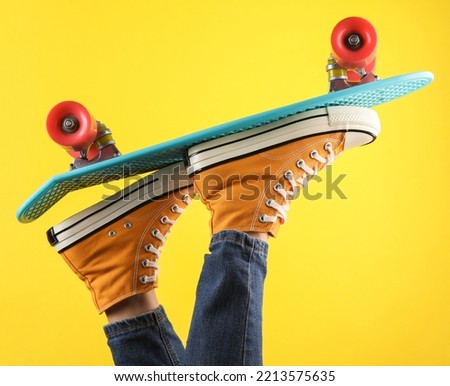 Female legs in retro 80s yellow sneakers and jeans on a penny board, yellow background