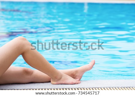 Female legs sitting by the blue swimming pool.