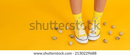 Female legs in socks with eggs and sneakers on yellow background with quail eggs