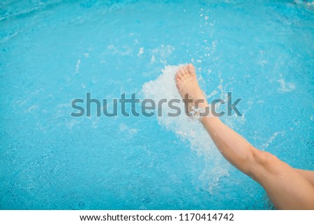 female legs splashing water in blue swimming pool, selective focus.