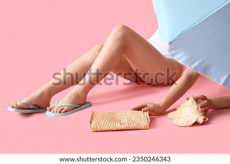 Female legs in stylish flip flops with beach accessories on pink background