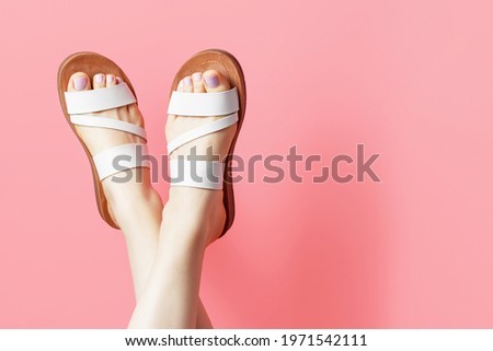 Female legs in summer flip flops on pink background, copy space