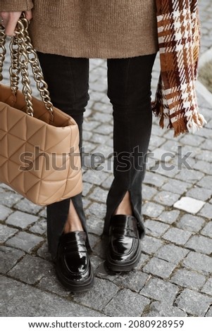 female legs in trendy black flared jeans with slits and loafers, caramel bag in hand, details of stylish autumn fashion outlook
