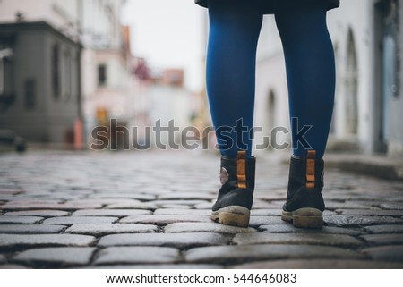 Female legs in trendy boots on cobblestone pavement, from ground back view