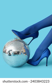 Female legs in trendy high heels with disco ball on blue background
