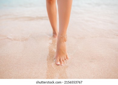 Female legs walking along the seaside barefoot, close-up of the perfect tanned legs of a girl coming out of the water after swimming. Woman relaxing on vacation, enjoying time at the beach, summer