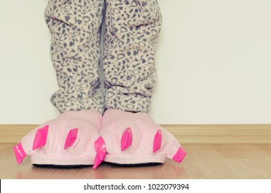 Female Legs In Warm Pajama And Cute Pink Monster Foot Slippers With Big Claws. Bedtime And Good Morning Concept.