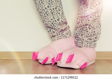 Female Legs In Warm Pajama And Cute Pink Monster Foot Slippers With Big Claws. Bedtime And Good Morning Concept.