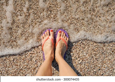 Female Legs Wearing Flip Flops Near Sea. Top View