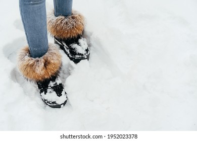 Female Legs Wearing Jeans And Warm Furry Boots Standing In A Snow