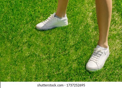 Female legs in white sneakers on a background on a green sports field. Sport concept, white sneakers for running on grass. Legs in professional sport shoes. Sport and fitness on fresh air