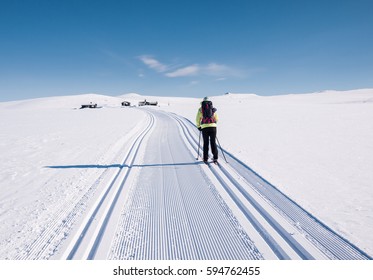 Female leisure cross-country skier alone in a well prepared double groomed track in the norwegian mountains at easter heading for a cluster of small cabins