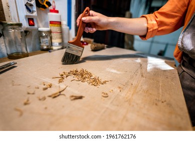 Female luthier cleaning wood chips from her worktable in traditional workshop. - Powered by Shutterstock