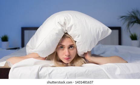 Female lying on bed and closing her ears with pillow - image