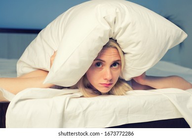 Female lying on bed and closing her ears with pillow - image