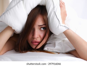 Female lying on bed and closing her ears with pillow.