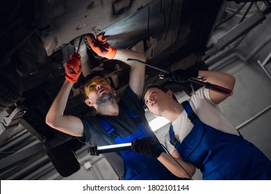 A Female Machinist Is Holding A Flashlight. Workman Repairing A Lifted Car