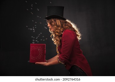 Female magician makes with soap bubbles show, an illusionist in theatrical clothes, on black background. Woman actress in stage costume. Concept of theatrical performance and fun show. Copy space