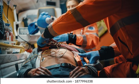 Female And Male EMS Paramedics Provide Medical Help To An Injured Patient On The Way To A Healthcare Hospital. Emergency Care Assistants Putting On Non-Invasive Ventilation Mask In An Ambulance.