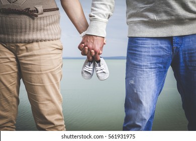 Female and male expecting a baby and holding each other's hands with a small pair of shoes in there