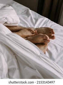 Female and male feet under blanket in bedroom