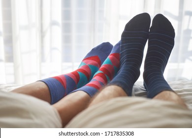 Female and male foot in socks on the bed enjoying sunny morning. 