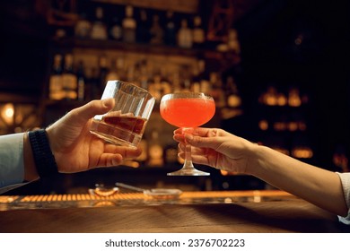 Female and male hands clinking glasses with alcoholic drinks closeup