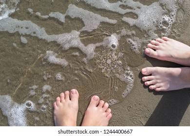 Female and male legs with huge sparkling snowflake on the sand in the sea foam. Concept of Winter and Christmas vacation on the beach and resort.