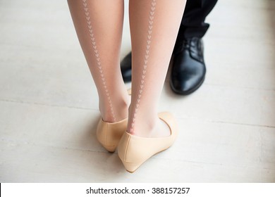 Female and male legs in rustic interior. Young woman dressed in cute white stockings with vertical line of little hearts drawing. Young couple in love standing together.