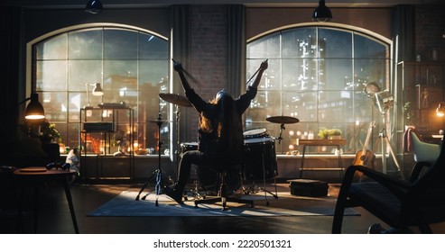 Female Or Male With Long Hair Sitting With Their Back To Camera, Playing Drums During An Evening Or Night Band Rehearsal In A Loft Studio. Heavy Metal Drummer Practising A Drum Solo Alone.