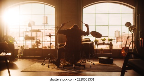 Female Or Male With Long Hair Sitting With Their Back To Camera, Playing Drums During A Band Rehearsal In A Loft Studio. Heavy Metal Drummer Practising A Drum Solo Alone.