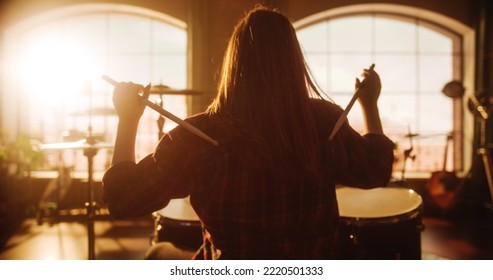 Female Or Male With Long Hair Sitting With Their Back To Camera, Playing Drums During A Band Rehearsal In A Loft Studio. Heavy Metal Drummer Practising Alone. Warm Color Editing.