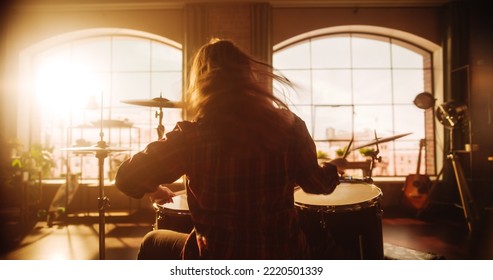 Female Or Male With Long Hair Sitting With Their Back To The Camera, Playing Drums During A Band Rehearsal In A Loft Studio. Heavy Metal Drummer Practising Alone. Warm Color Editing.