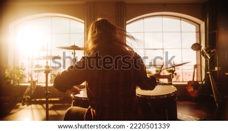 Female or Male with Long Hair Sitting with Their Back to the Camera, Playing Drums During a Band Rehearsal in a Loft Studio. Heavy Metal Drummer Practising Alone. Warm Color Editing.