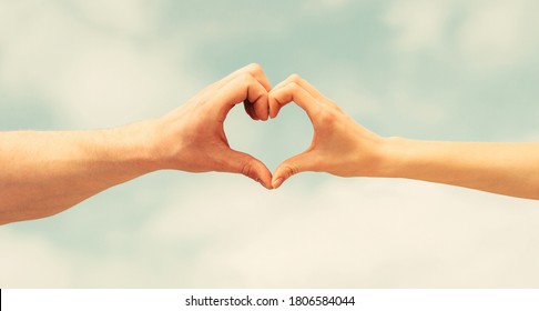 Female and man hands in the form of heart against the sky. Hands in shape of love heart. Heart from hands on a sky background.
