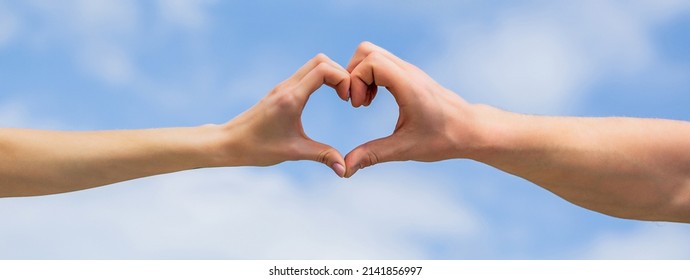 Female and man hands in the form of heart against the sky. Hands in shape of love heart. Heart from hands on a sky background. Love, friendship concept. Girl and male hand in heart form love blue sky.